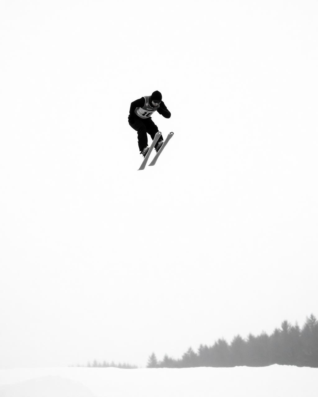 Schwarzweiße Aufnahme eines Skispringers im Flug vor leerem Winterhimmel